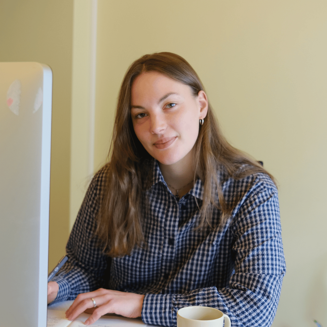 Personen på bildet sitter ved et skrivebord med en datamaskin, notisbok og kaffekopp. «KI-generert bildetekst, kvalitetssikret før publisering.» 