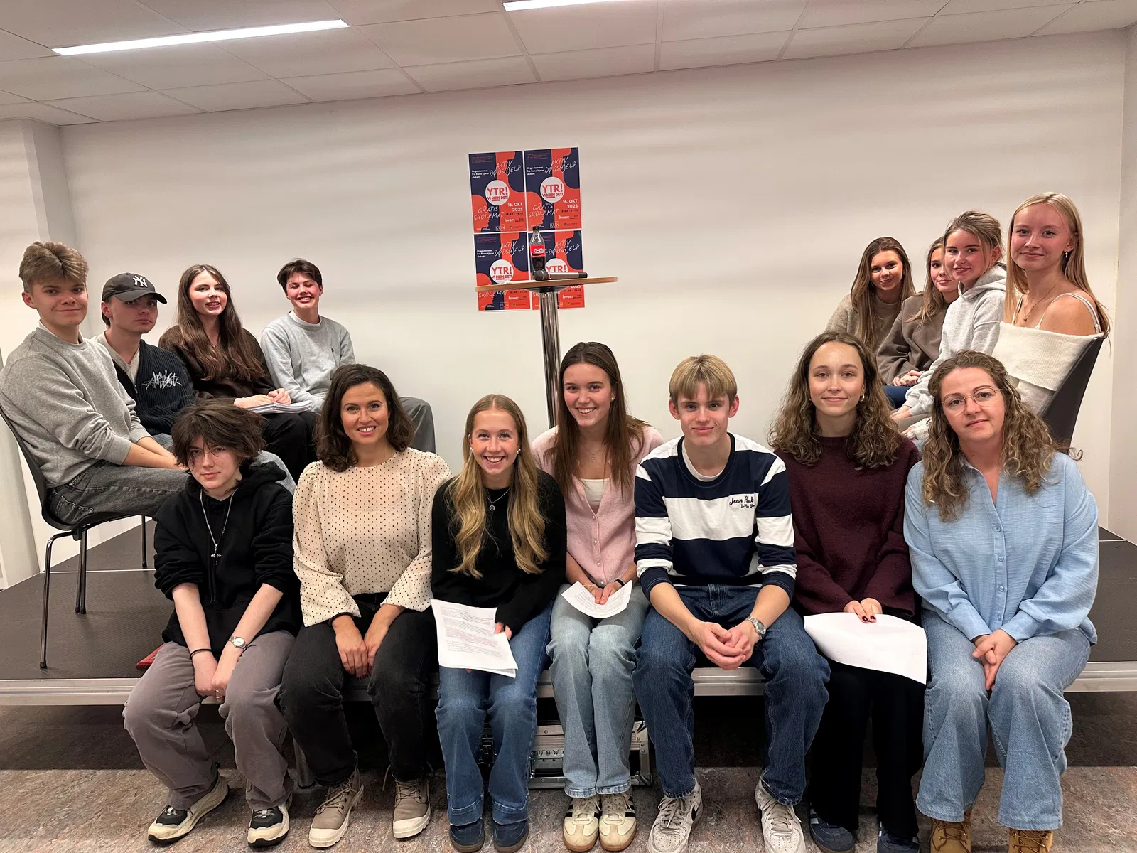 Bildet viser en gruppe mennesker som sitter og står foran en plakat. Det er både unge og voksne deltakere. Stemningen virker vennlig og avslappet. «KI-generert bildetekst, kvalitetssikret før publisering.» 