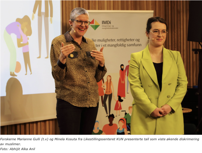Bildet viser to personer (seniorrådgivere på KUN, Marianne og Minela) som står foran en plakat med IMDis logo. Den ene personen snakker inn i en mikrofon, mens den andre lytter. De ser ut til å være på en presentasjon om diskriminering av muslimer. «KI-generert bildetekst, kvalitetssikret før publisering.»