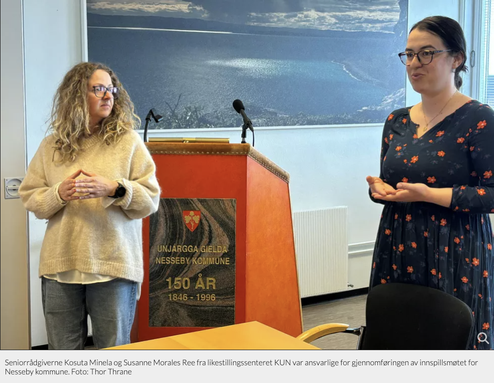 Seniorrådgivere Minela Košuta og Susanne Morales Ree fra likestillingssenteret KUN står ved en talerstol i et rom, begge ser engasjerte ut. Bakgrunnen viser en dekorasjon for Unjárgga gielda / Nesseby kommune. «KI-generert bildetekst, kvalitetssikret før publisering.»