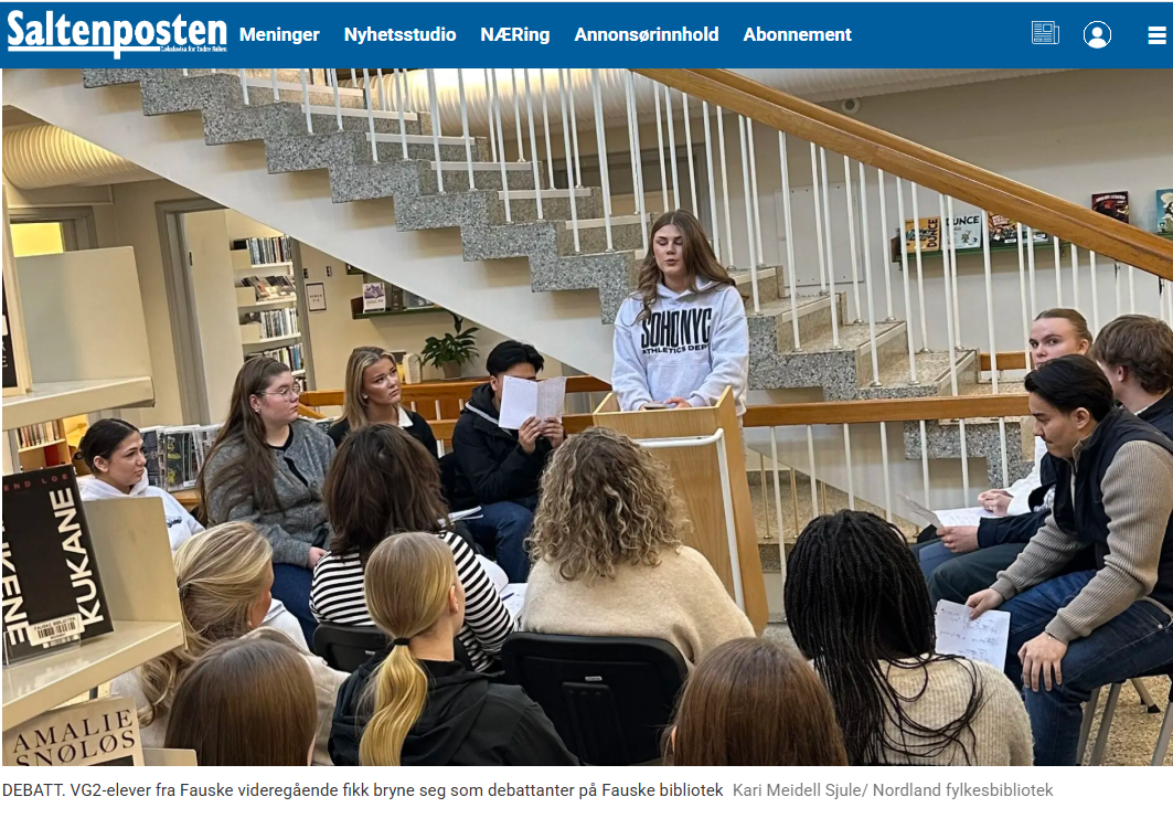 Bildet viser en gruppe elever fra Fauske videregående skole som deltar i en debatt på Fauske bibliotek. En av elevene står ved en talerstol, mens de andre sitter i en halvsirkel rundt. Det ser ut til å være en engasjerende diskusjon i en biblioteksetting med trapper i bakgrunnen.  «KI-generert bildetekst, kvalitetssikret før publisering.»